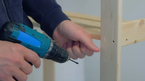 Man screws boards using electric screwdriver collecting rack furniture bookcase. Stock Footage 129590965
