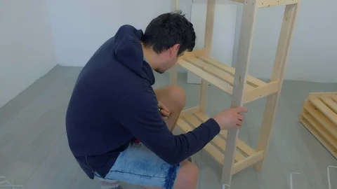 Man screws boards using electric screwdriver collecting rack furniture bookcase. Stock Footage 129591076