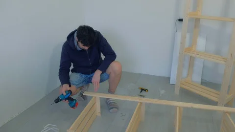 Man screws parts using electric screwdriver collecting rack furniture bookcase. Stock-Footage 129591279