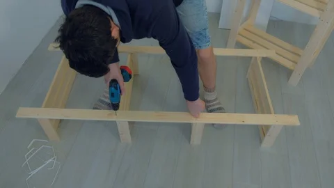 Man screws parts using electric screwdriver collecting rack furniture bookcase. Video stock 129591878
