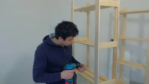 Man screws partss using electric screwdriver collecting rack furniture bookcase. Stock Footage 129592894