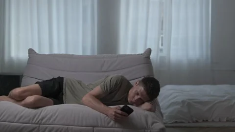Man scrolling smartphone on sofa at home, concept of phone addiction and social Stock Footage 311762914