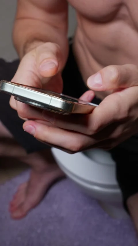 Man Scrolling on Smartphone While Sitting on Toilet Seat at Home Stock Footage 339210484
