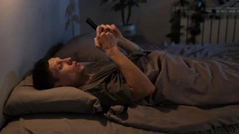 Man scrolling through his phone in bed at night, unwinding after a long day. Stock Footage 296057982
