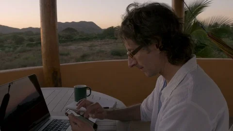 Man scrolling through smart phone at home office by ocean looking at email Stock Footage 80137333