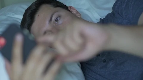 Man Scrolls through Phone Lying Sick in Bed Stock Footage 114703771
