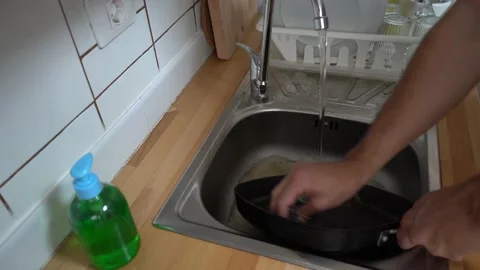 A man scrubbing a frying pan in the kitchen sink Stock Footage 147555430