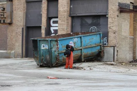 Man Searching Backpack in Front of Dumpster Foto stock