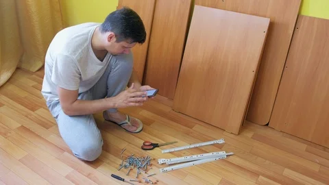 Man is searching in internet on smartphone how to collect the table from parts. Video stock 124856728