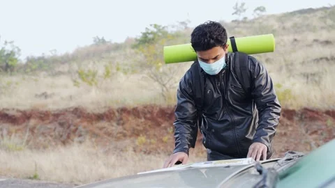 Man is searching map by placing on car bonnet with wearing mask Stock Footage 146221960