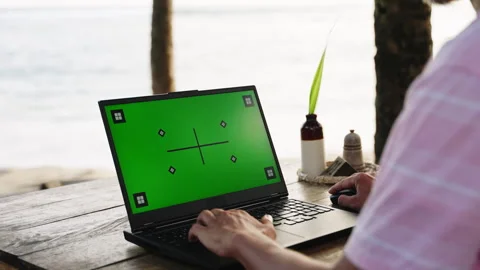 Man at seaside cafe works on laptop with green screen. Freelancer uses pc for Stock Footage 302251992