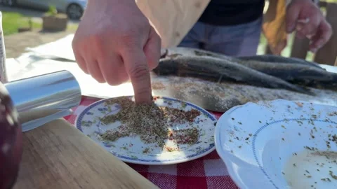 Man Seasoning Fresh Fish on Rustic Outdoor Table in Countryside Stock Footage 333523315
