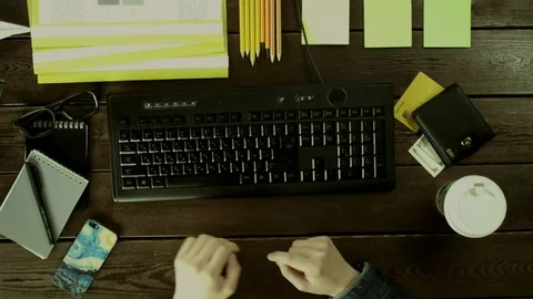 A man seat near a computer keyboard on his desk and and takes a notebook to Stock Footage 82011159