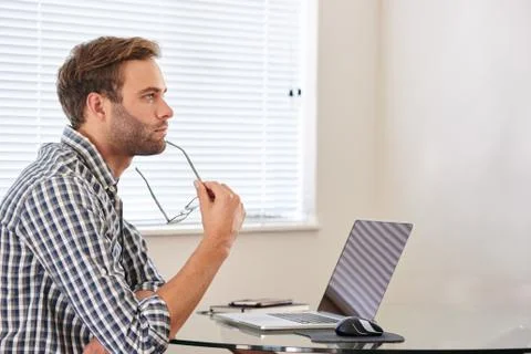 Man seated behind computer looking into the distance in thought Stock Photos