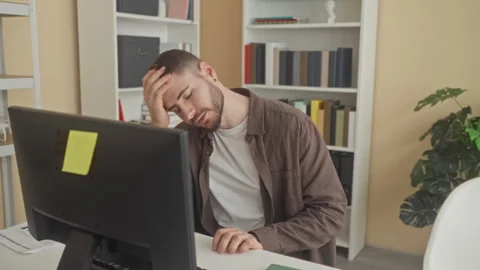 Man seated at computer, rubbing his temples with hands and adjusting collar.. Stock Footage 347815627