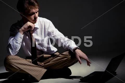 Man seated inside dark room in front of laptop pointing at its monitor Stock Photos