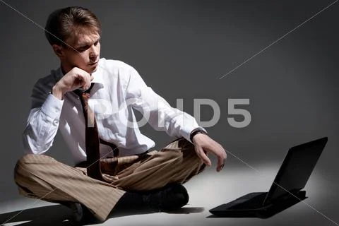 Man seated inside dark room in front of laptop looking at its monitor Stock Photos