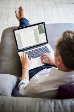 A man seated on a sofa, using a laptop computer, over the shoulder view. Stock Photos