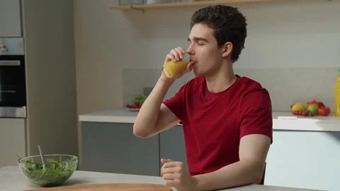 A man is seated at a table, holding a cup and drinking orange juice. 스톡 동영상 274551164