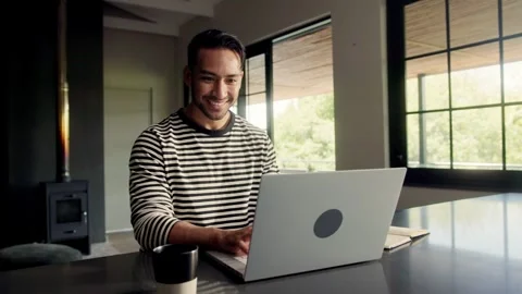 Man seated at a table, using a laptop computer inside a building with a window Stock Footage 273777916