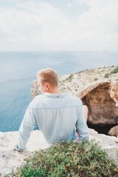 A man seating in front of a large rock. Watching to the sea. Nice weather. Stock Photos