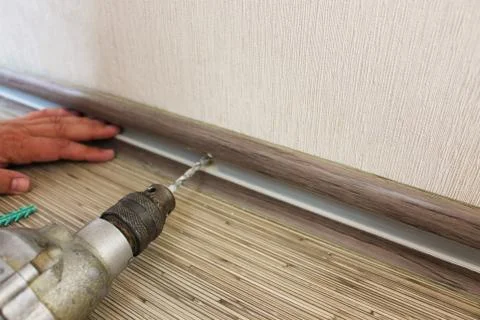 The man secures the baseboard to the wall Stock Photos