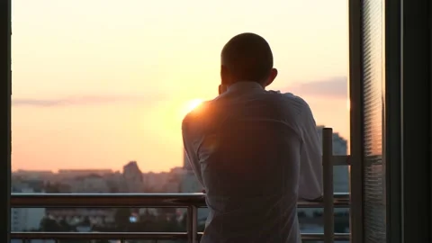 A man sees off the sunset standing on a balcony overlooking the city, close-up Stock Footage 202321773