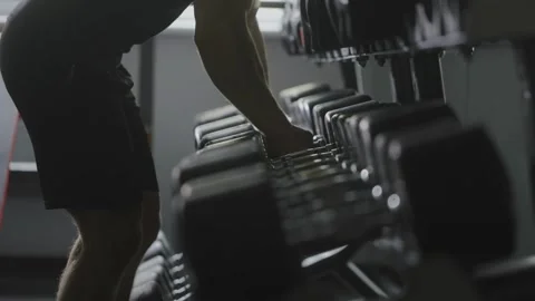 Man selecting Dumbbell Rack in Gym Exercising Equipment for Effective Workout Stock Footage 256751182