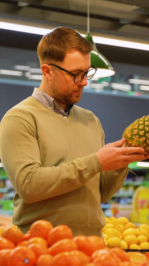 Man selecting grapefruit, pineapple, and bananas in supermarket Stock Footage 304089135