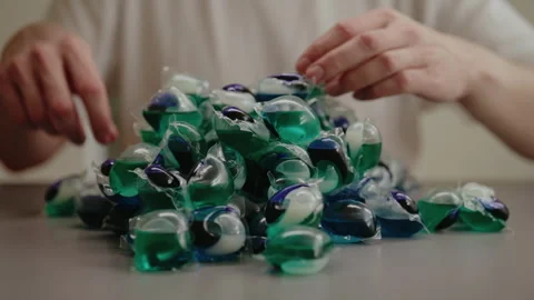 Man selecting laundry detergent pod from large pile of colorful pods sitting at Stock Footage 311564172