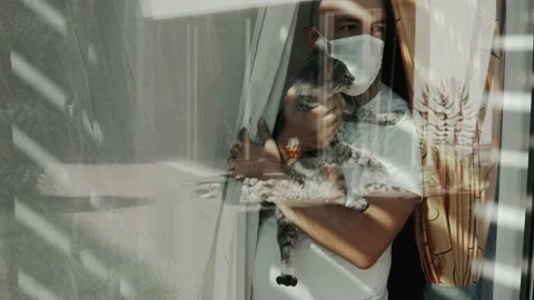 Man in self isolation looking out of the window with a cat 動画素材 138901600