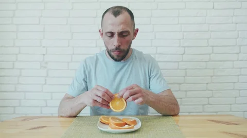 Man in self-isolation. A man eating orange and licks his fingers. A man is Stock Footage 128438016