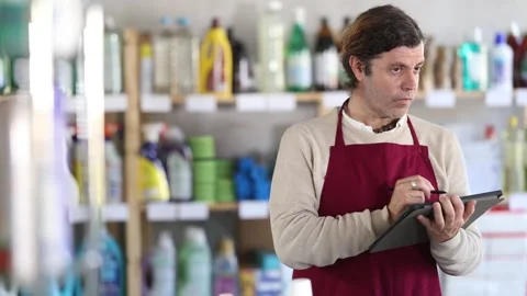Man seller, with tablet in hands, make inventory in store. Seller counts number Stock Footage 313459227