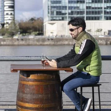 A man sending messages while smiling at a bar near the river Stock Photos