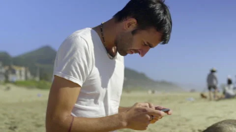 Man sending text messages sitting in the sand at the beach. Stock Footage 52257991