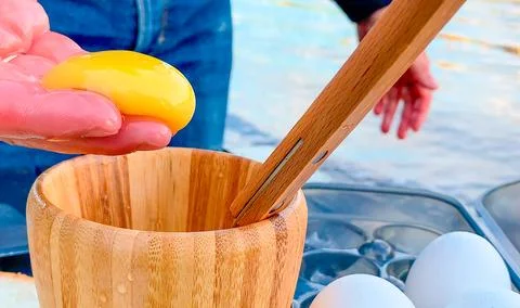 A man separates an egg yolk from the white and holds the yolk in his palm Stock Photos