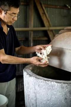 A man separating pieces of vegetable fibres above a vat, ingredient of Stock Photos