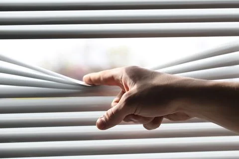 Man separating slats of white blinds indoors, closeup Fotos de archivo