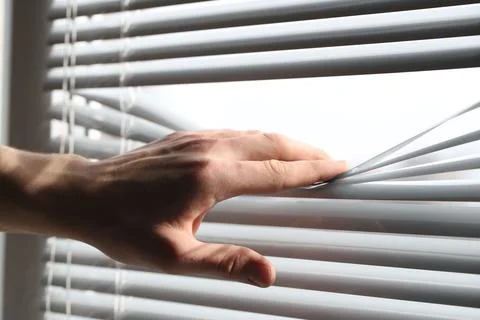 Man separating slats of white blinds indoors, closeup Fotos de archivo
