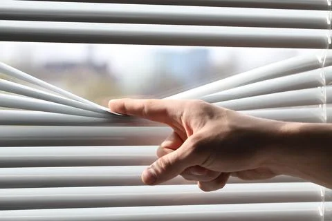 Man separating slats of white blinds indoors, closeup Stock Photos