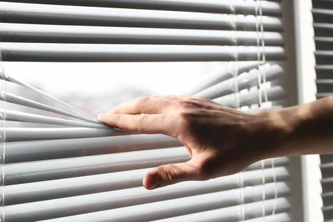 Man separating slats of white blinds indoors, closeup Fotos de archivo