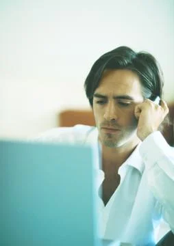 Man with serious expression using cellphone while looking at laptop computer Stock Photos