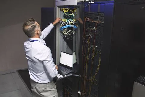 Man, server and wire with laptop in data center for programming, coding and Stock Photos