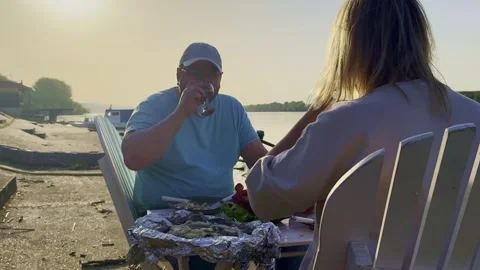 Man Serving Grilled Fish at Riverside Picnic Table Video stock 334134380