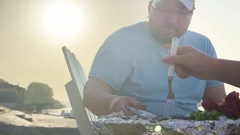 Man Serving Grilled Fish at Riverside Picnic Table Stock Footage 334134709