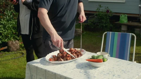Man serving grilled meat on plate at backyard garden table, family barbecue Video stock 329232747