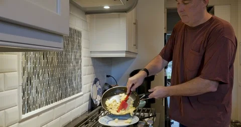 Man serving scrambled eggs on to a plate with a silicone spatula Stock Footage 109072866