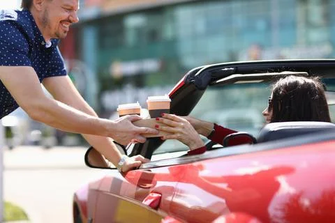 Man serving two glasses of coffee to woman in red convertible Stock Photos