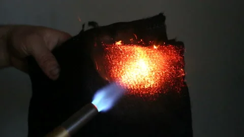 A man sets fire to a black fireproof fabric with a gas burner. Real time, contai Stock Footage