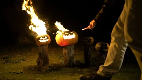 Man sets fire to halloween pumpkins on tree log in darkness, field, mist, dusk Stock-Footage 81572551